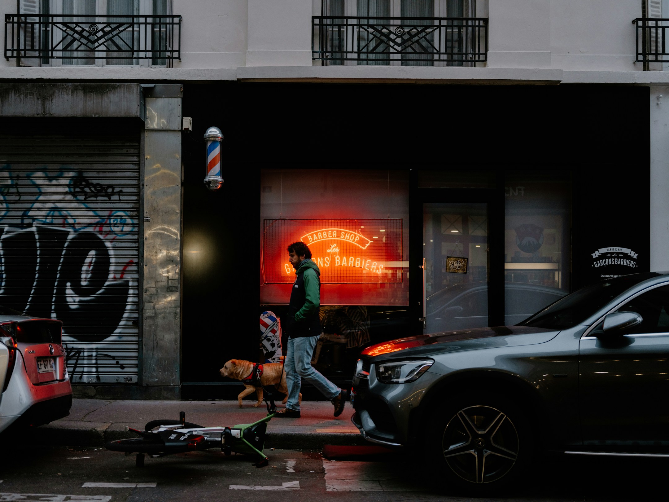 A barbershop neon sign glowing at night, a person walking past with a dog. The kind of moment where calls get missed.