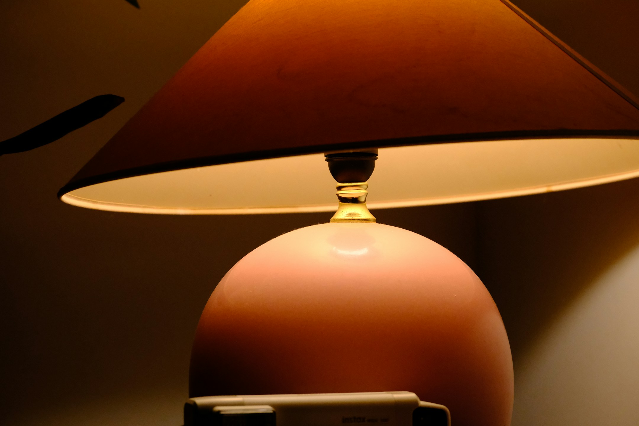 A pink table lamp on a wooden surface beside a notebook, the warmth of a quiet evening when the day is finishing up.