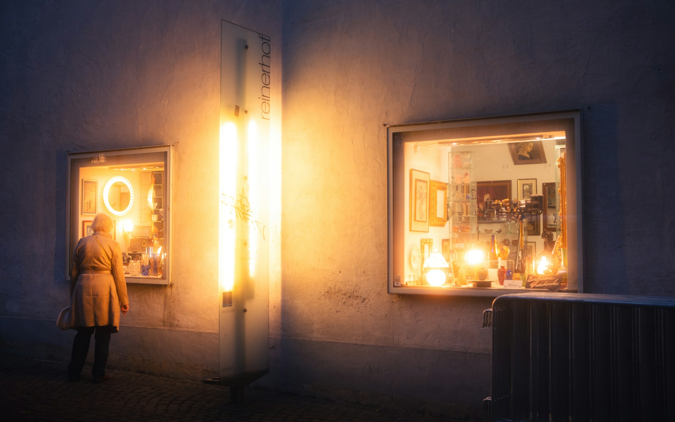 A window-shop view at night, soft glow inside, the visual of presence without entering.
