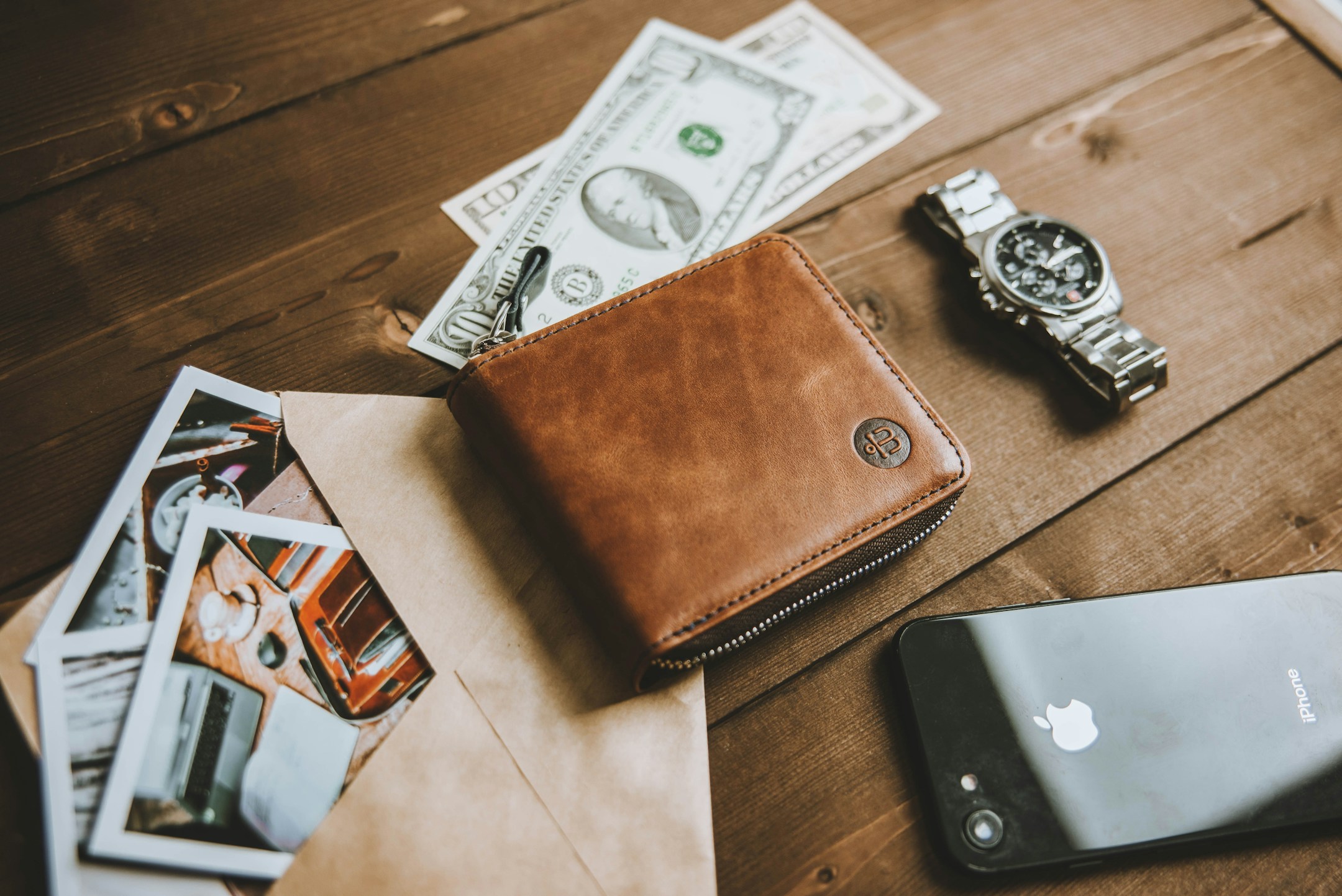 A wallet, a phone, and keys on a clean wooden table, the personal items at the moment of paying for something.