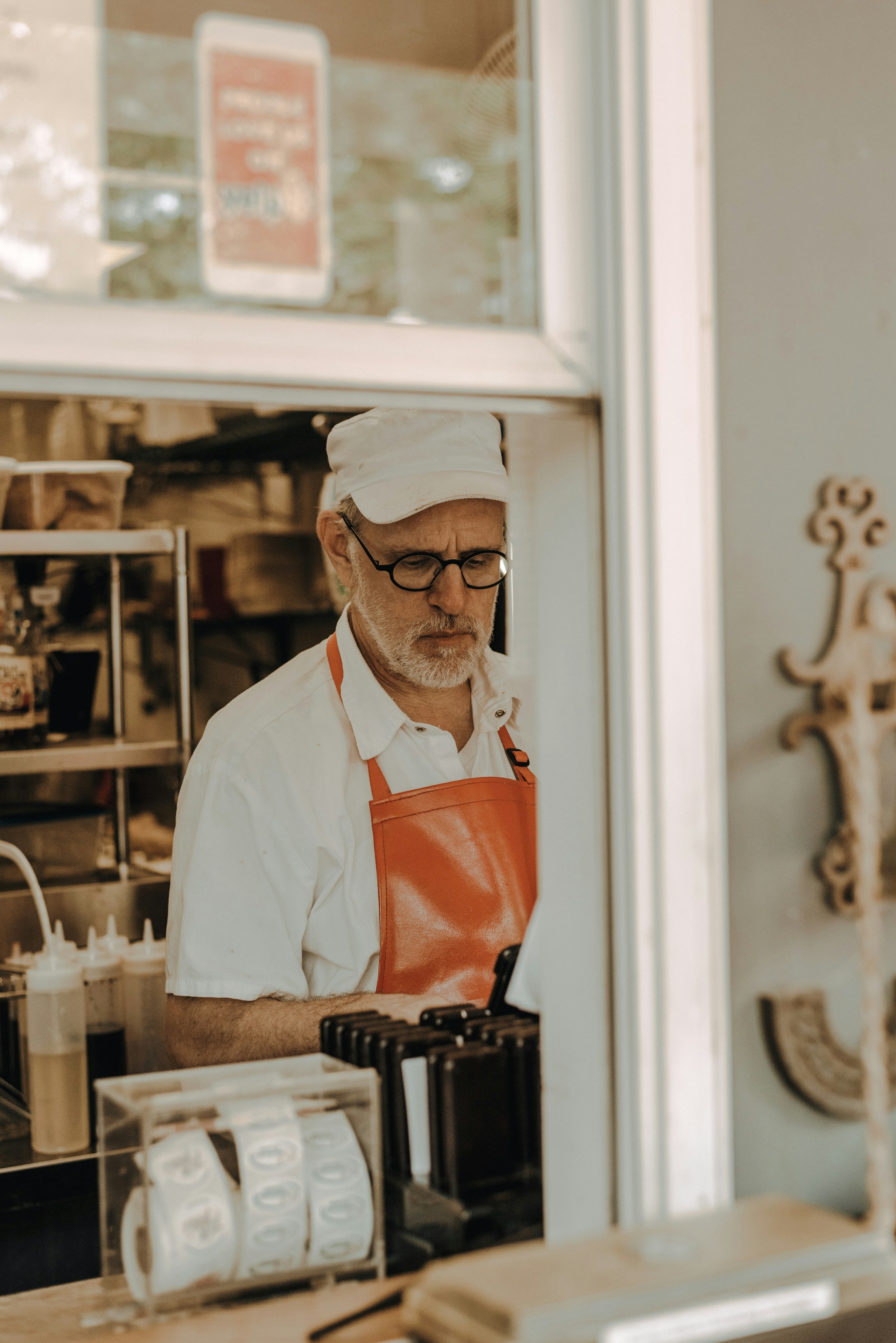 A baker in a white cap. A morning rush is starting and the bakery's phone is ringing.