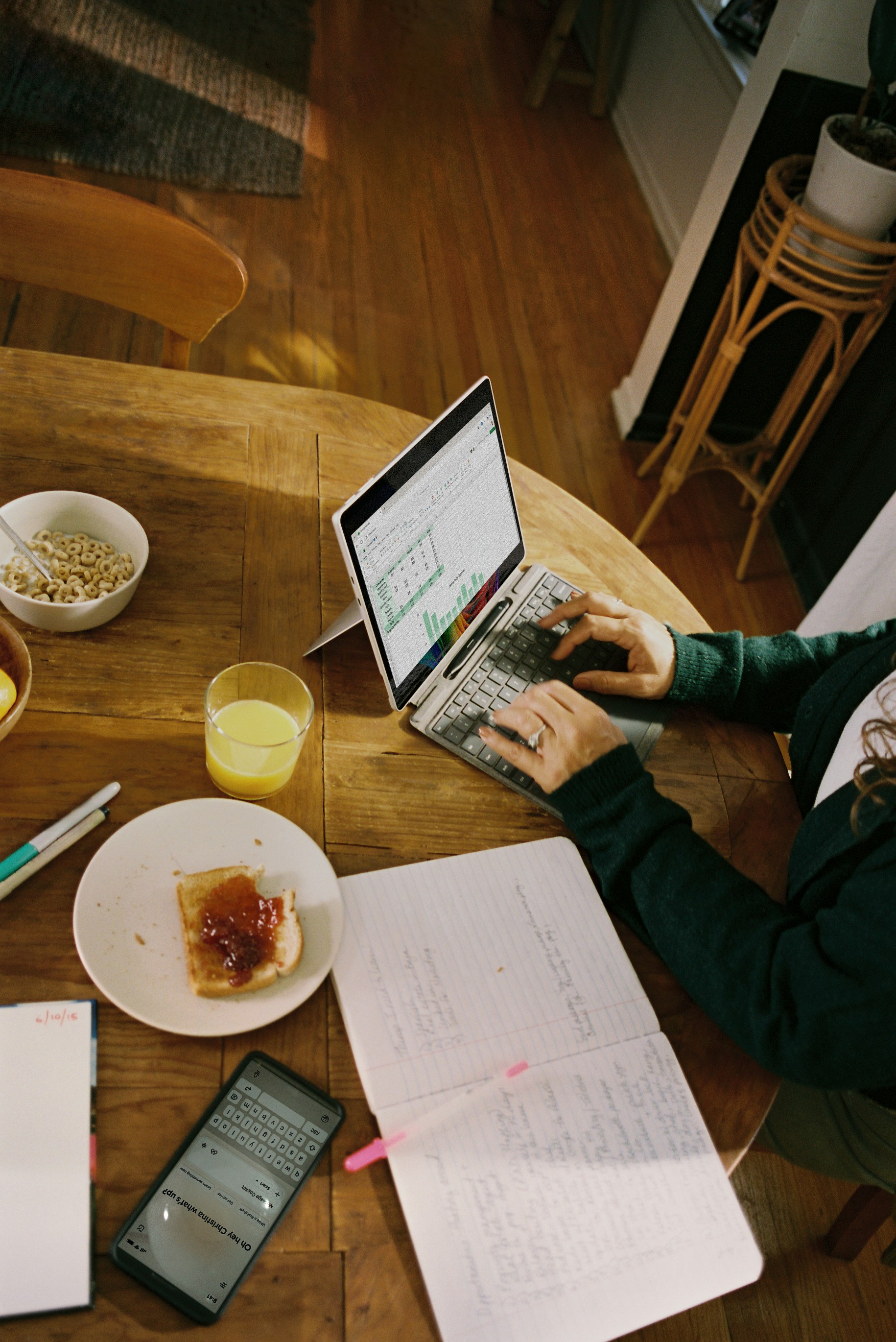 An overhead shot of a creator at a wooden table with toast, juice, a laptop, and a notebook.