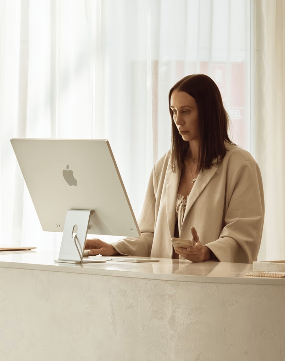 A small-business owner at her iMac desk in a calm, minimal workspace.