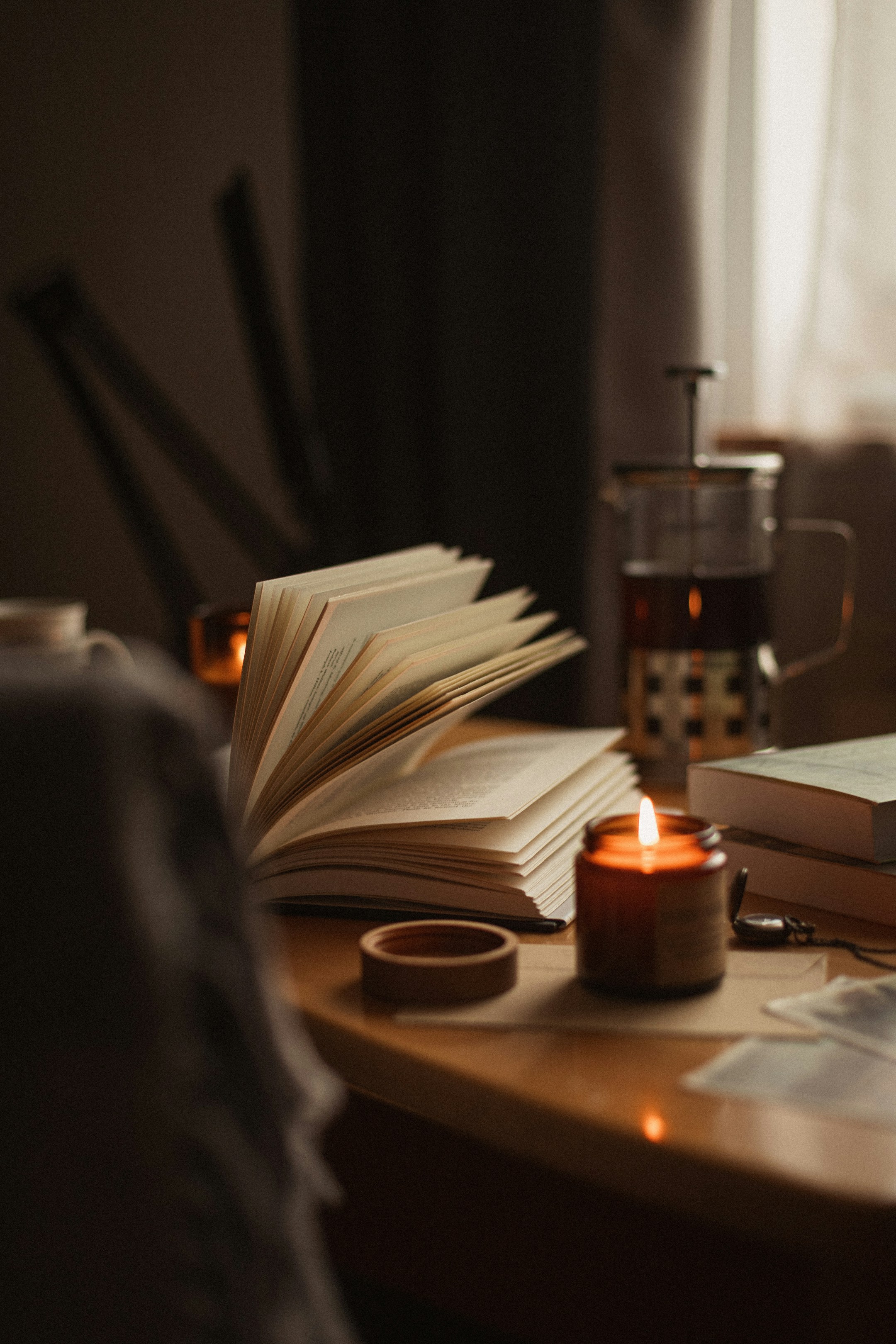 A book, a candle, and a French press in low warm light. The hour the agent gave back.